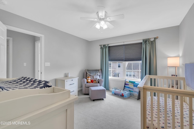 bedroom with a ceiling fan, a nursery area, and light colored carpet