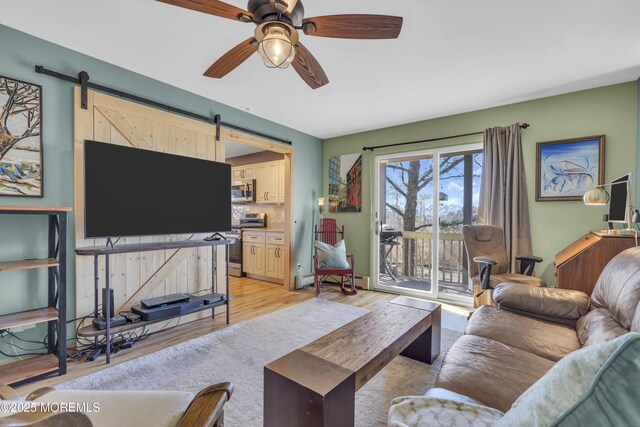 living room with light wood-type flooring, a barn door, and ceiling fan