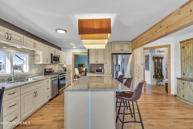 kitchen with light wood finished floors, a breakfast bar, a sink, appliances with stainless steel finishes, and a center island