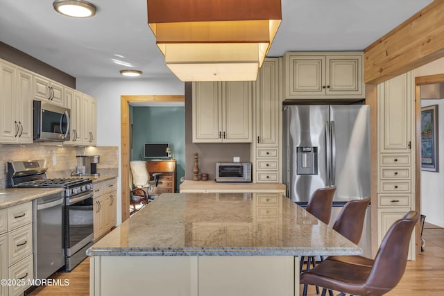 kitchen with tasteful backsplash, a center island, light stone countertops, a kitchen breakfast bar, and stainless steel appliances