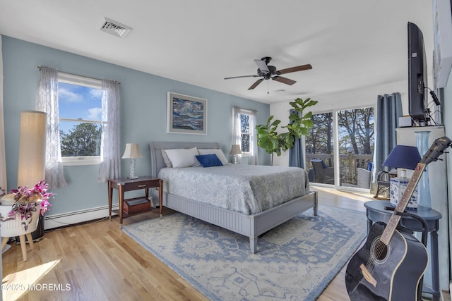 bedroom with multiple windows, light wood-style floors, visible vents, and a baseboard radiator