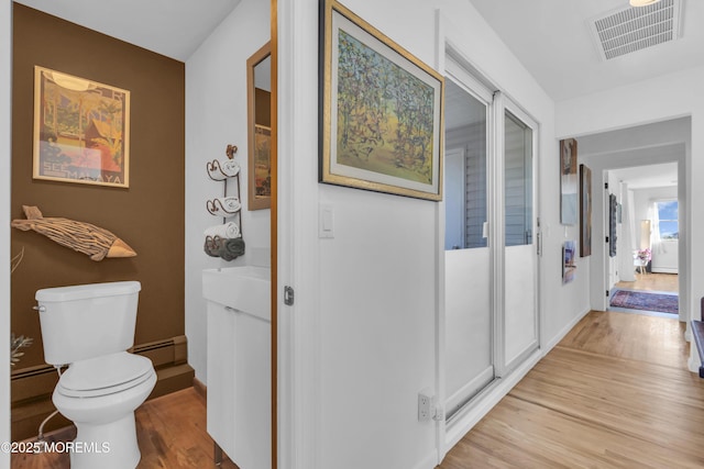 hall featuring visible vents, baseboards, a baseboard heating unit, and light wood finished floors