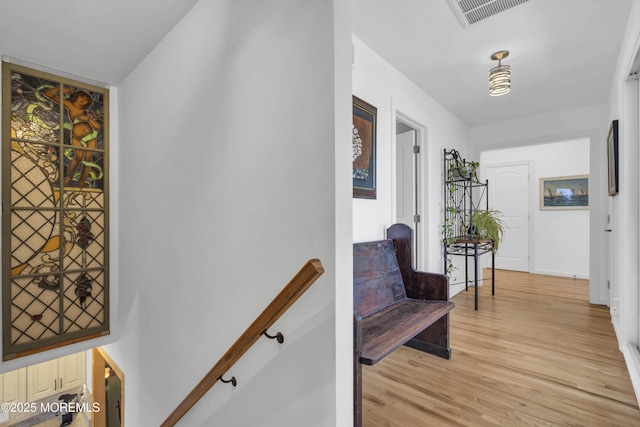 hallway with an upstairs landing, visible vents, and light wood finished floors