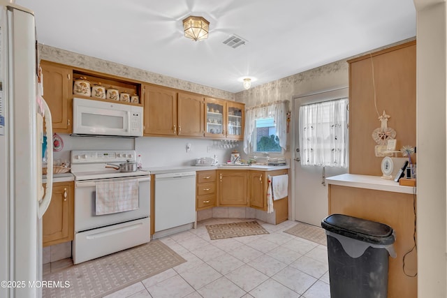 kitchen featuring light tile patterned floors, light countertops, visible vents, glass insert cabinets, and white appliances