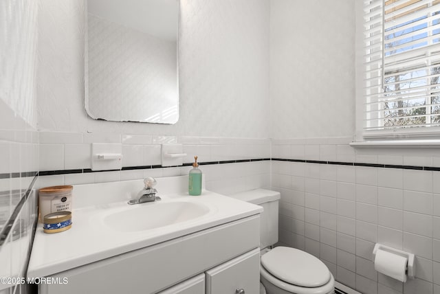 bathroom with toilet, wainscoting, vanity, and wallpapered walls