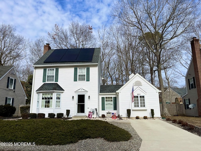 colonial home with a chimney, solar panels, and roof with shingles