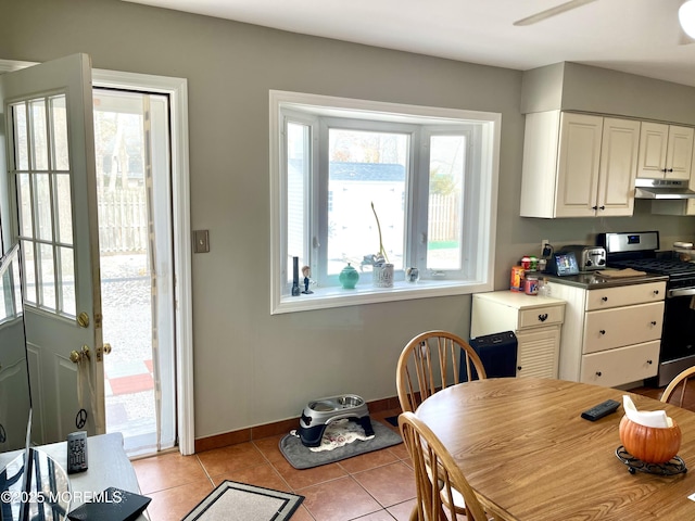 kitchen featuring baseboards, gas stove, dark countertops, under cabinet range hood, and light tile patterned flooring