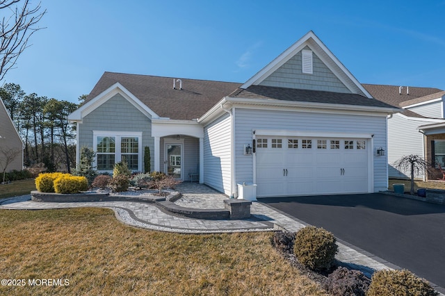 ranch-style house with aphalt driveway, roof with shingles, an attached garage, and a front lawn