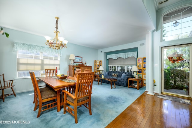 carpeted dining area featuring visible vents, baseboards, ornate columns, wood-type flooring, and an inviting chandelier