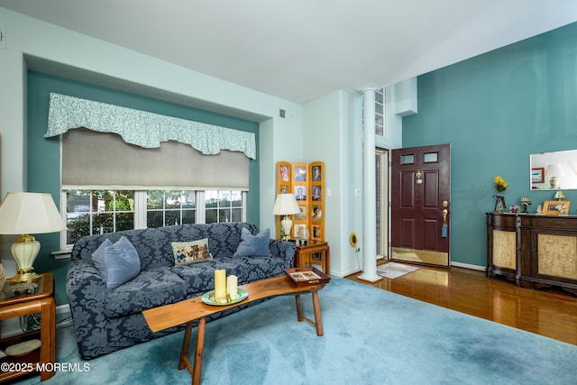 living area with decorative columns, visible vents, baseboards, and wood finished floors