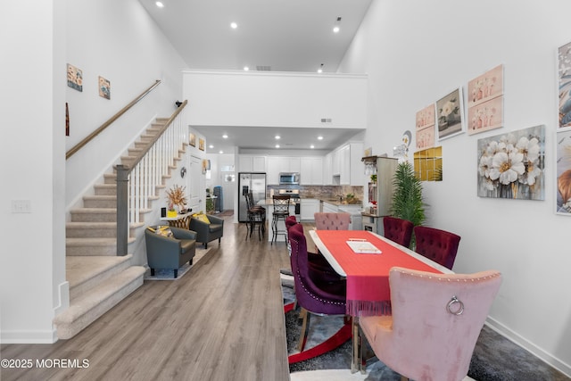 dining room featuring visible vents, light wood-style flooring, a high ceiling, and stairs