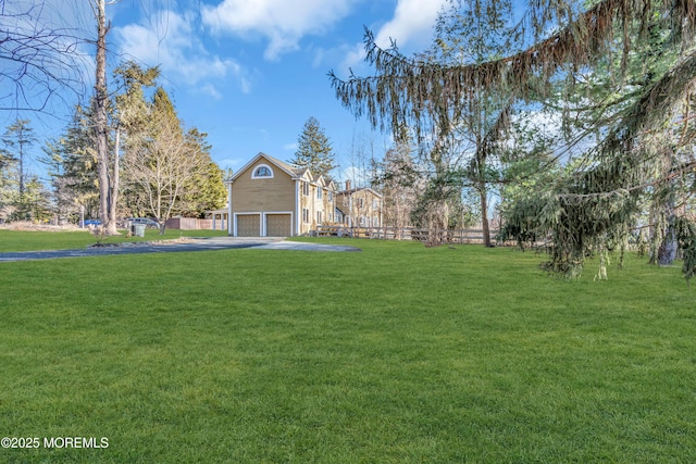 view of yard featuring aphalt driveway, an attached garage, and fence