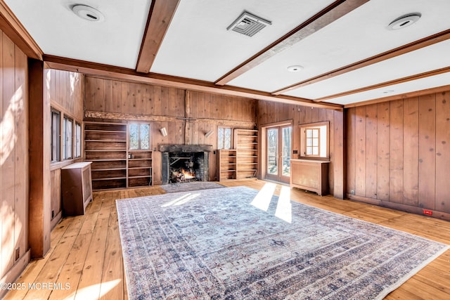 unfurnished living room with a fireplace with flush hearth, visible vents, light wood-style flooring, and beam ceiling