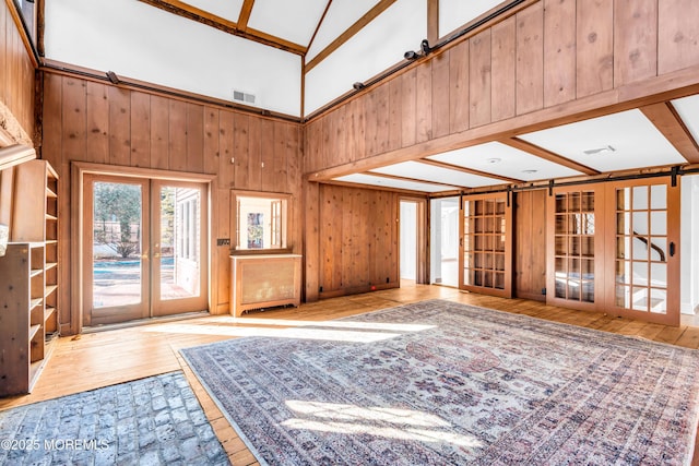 living room with french doors, visible vents, wooden walls, and hardwood / wood-style flooring