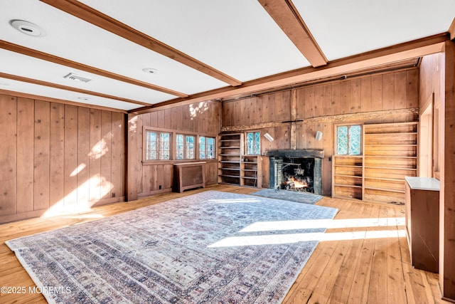 living area with wood-type flooring, visible vents, wood walls, beamed ceiling, and a lit fireplace