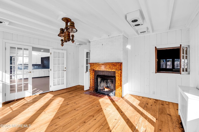 unfurnished living room with a fireplace, visible vents, light wood-style floors, french doors, and beam ceiling