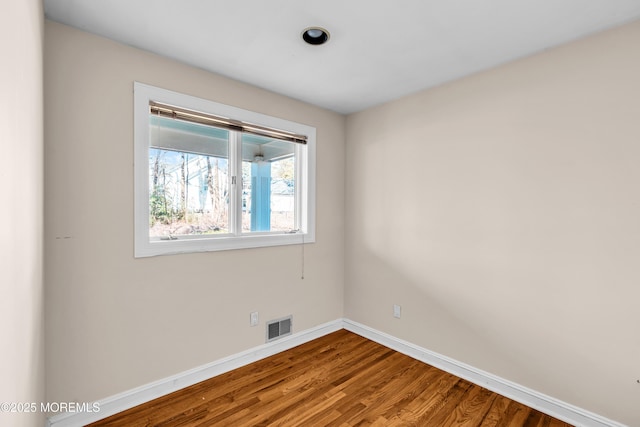 spare room featuring baseboards, visible vents, and wood finished floors