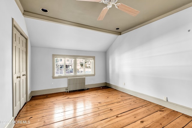 spare room with baseboards, vaulted ceiling, radiator, light wood finished floors, and crown molding