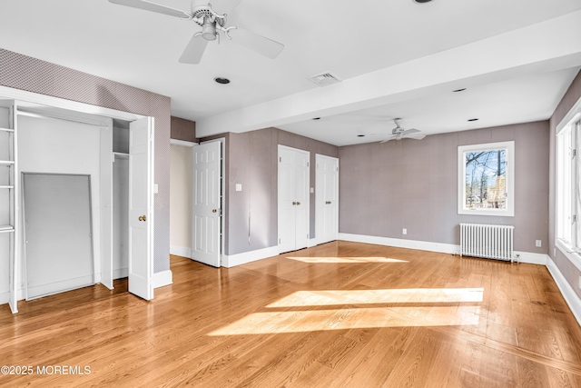 unfurnished bedroom featuring visible vents, baseboards, radiator heating unit, light wood-style flooring, and two closets