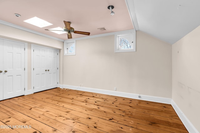 interior space with light wood finished floors, lofted ceiling with skylight, visible vents, and baseboards