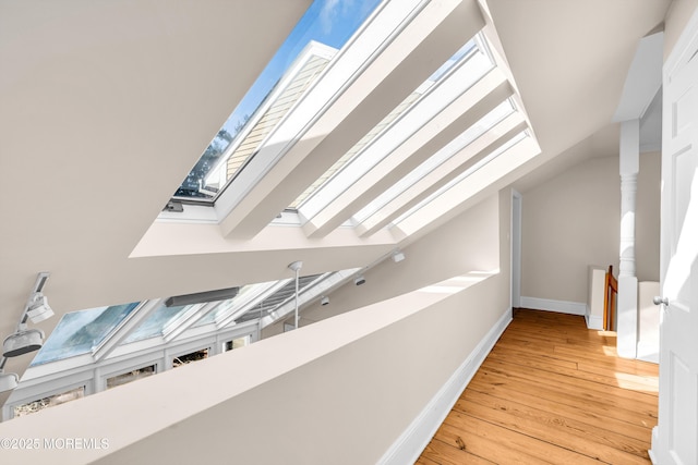 additional living space featuring vaulted ceiling with skylight, baseboards, and wood finished floors