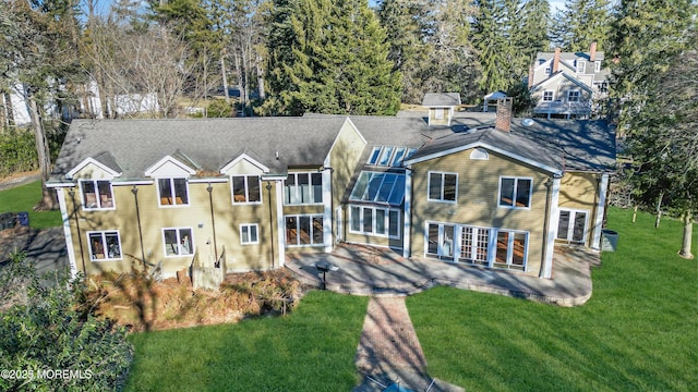 rear view of property featuring a lawn, a balcony, a chimney, french doors, and a patio area