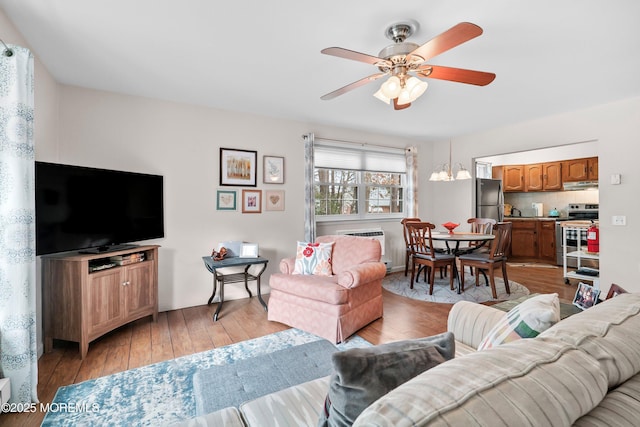 living room featuring light wood-type flooring, a wall mounted AC, and ceiling fan with notable chandelier