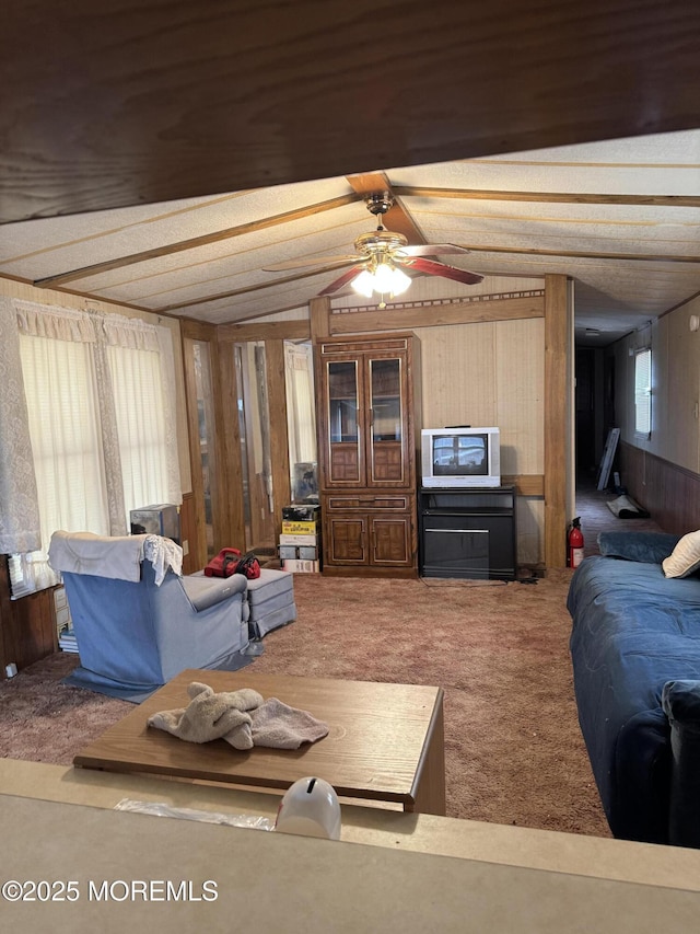 living room featuring vaulted ceiling with beams, carpet flooring, a ceiling fan, and wooden walls