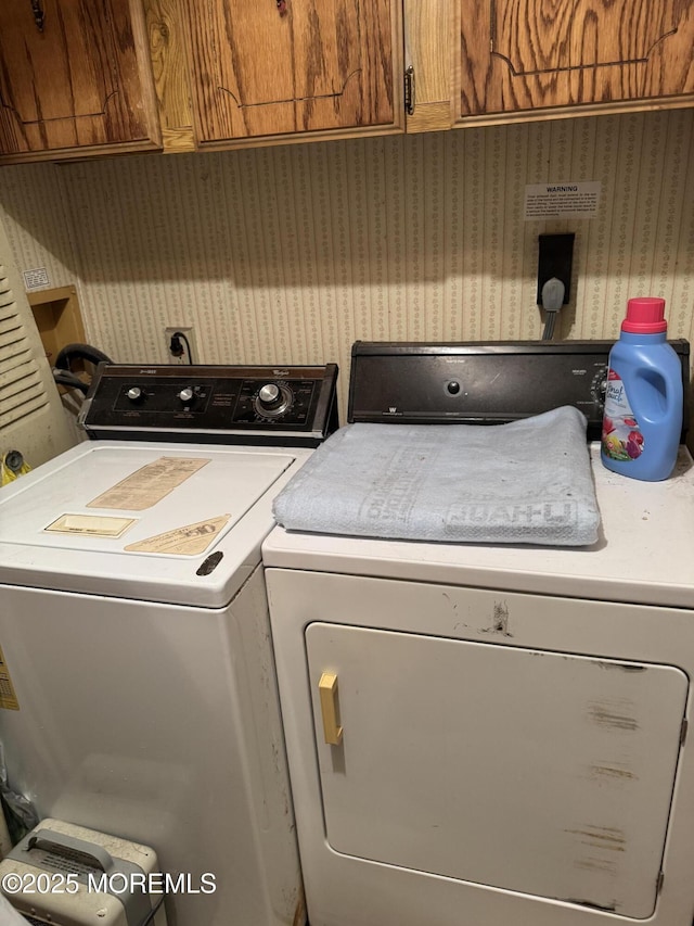 clothes washing area with washer and clothes dryer, cabinet space, and wallpapered walls