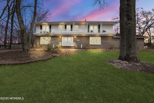 rear view of property with french doors, brick siding, a lawn, and a balcony