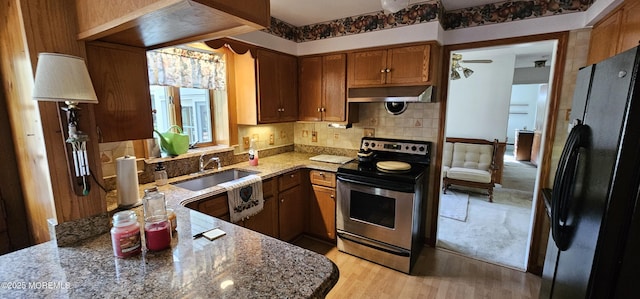 kitchen featuring stainless steel electric range oven, a sink, light stone counters, freestanding refrigerator, and extractor fan