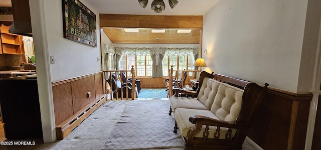 living area with wooden walls, carpet flooring, baseboard heating, a wainscoted wall, and a baseboard radiator