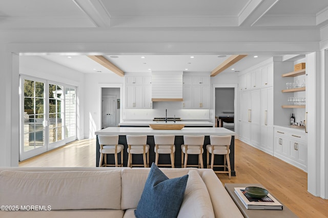 kitchen featuring light countertops, a sink, beam ceiling, and white cabinetry