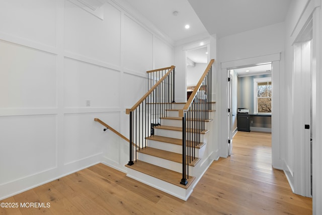 stairs with ornamental molding, a decorative wall, hardwood / wood-style floors, and recessed lighting