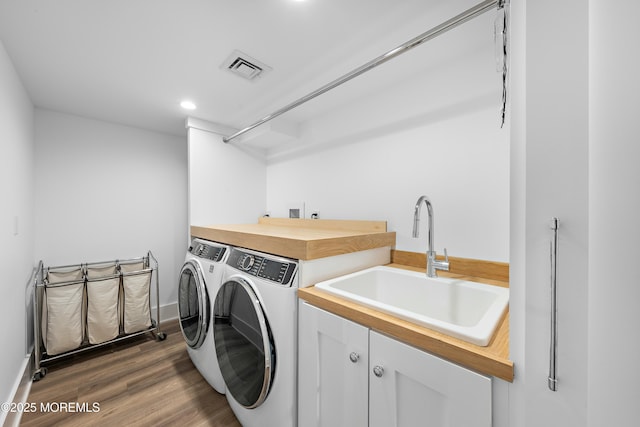 clothes washing area with washing machine and dryer, a sink, visible vents, cabinet space, and dark wood finished floors