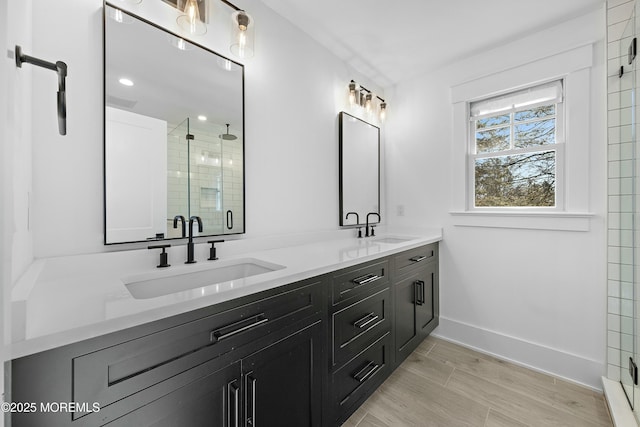 full bath featuring baseboards, double vanity, a sink, and a shower stall