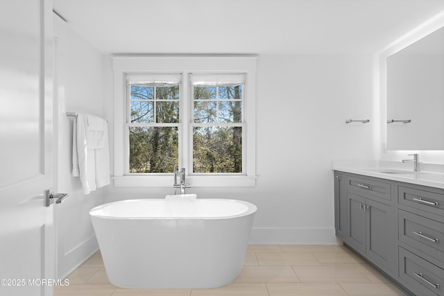 bathroom with a soaking tub, tile patterned floors, baseboards, and vanity