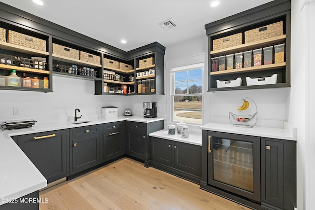 bar featuring light wood-style flooring, recessed lighting, a sink, visible vents, and indoor wet bar