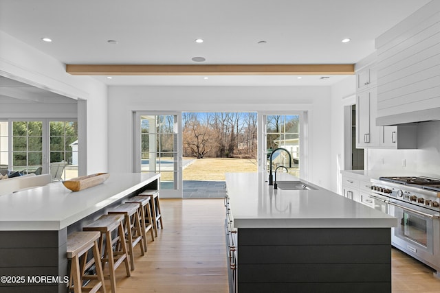 kitchen featuring light wood-style flooring, a sink, white cabinetry, double oven range, and a large island with sink