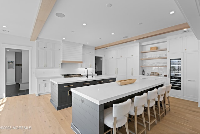 kitchen with white cabinets, a large island with sink, and beamed ceiling