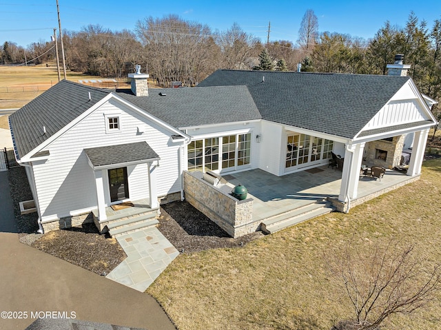 rear view of house featuring a yard, a chimney, a patio, and roof with shingles