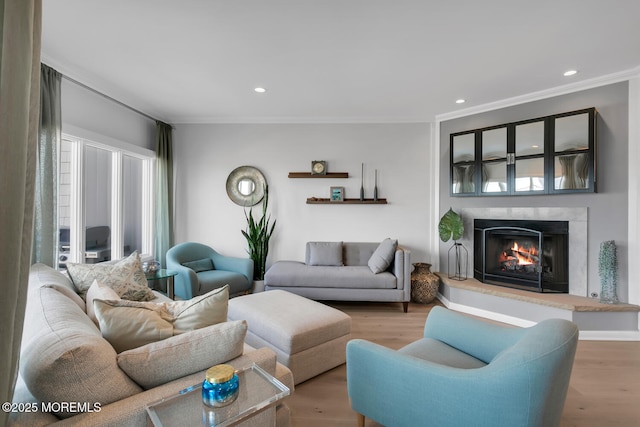 living area featuring a lit fireplace, ornamental molding, wood finished floors, and recessed lighting