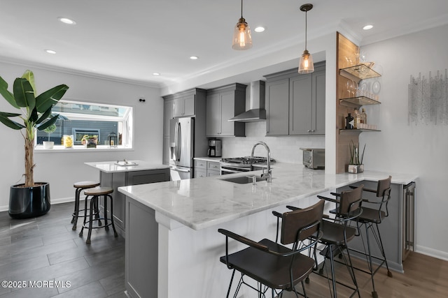 kitchen with a breakfast bar, gray cabinetry, appliances with stainless steel finishes, a sink, and wall chimney exhaust hood