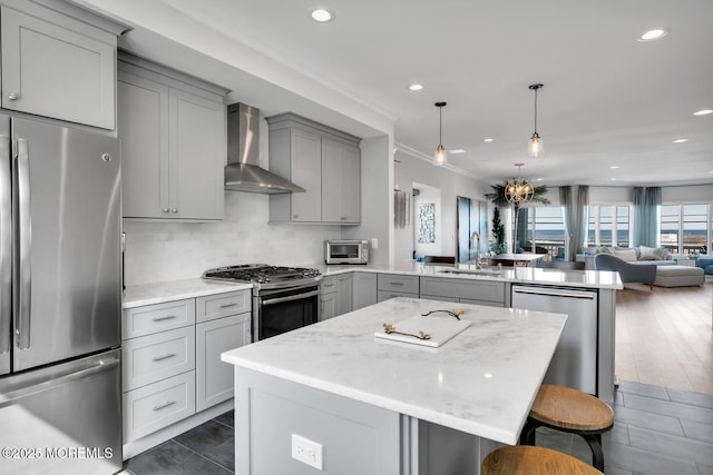 kitchen featuring a peninsula, wall chimney range hood, gray cabinets, and stainless steel appliances