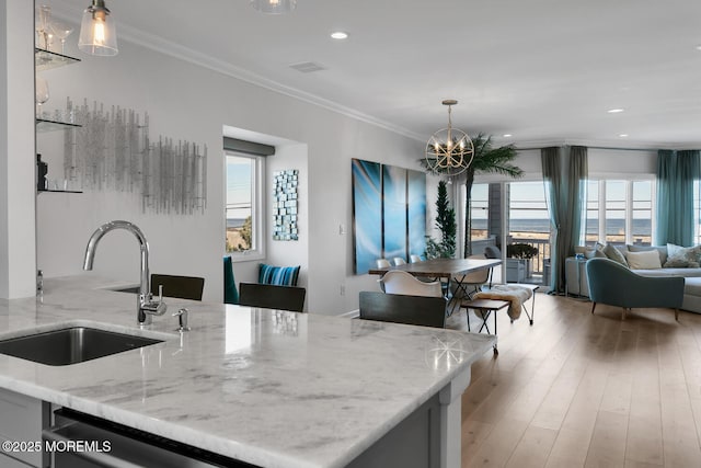 kitchen with light wood finished floors, ornamental molding, open floor plan, light stone countertops, and a sink