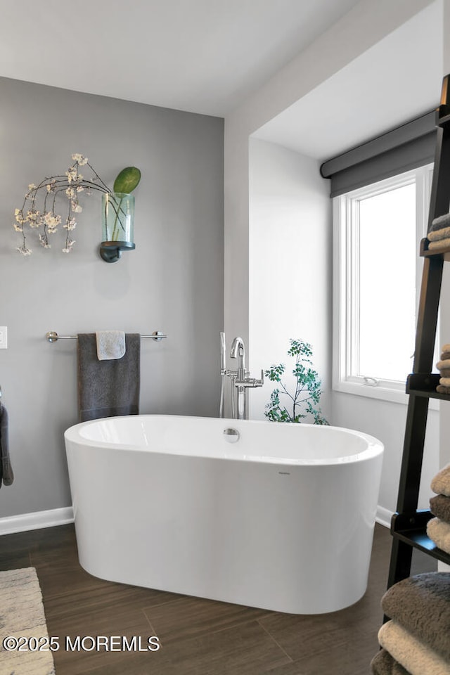 full bathroom featuring a freestanding bath, baseboards, and wood finished floors