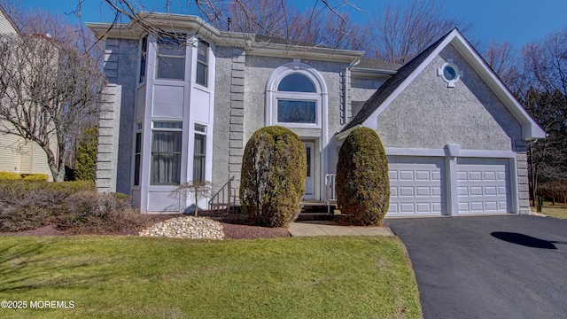 view of front facade featuring an attached garage, driveway, a front yard, and stucco siding