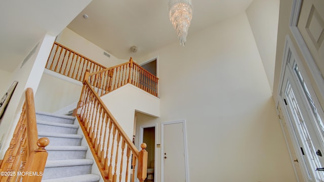 staircase with visible vents, a towering ceiling, and an inviting chandelier