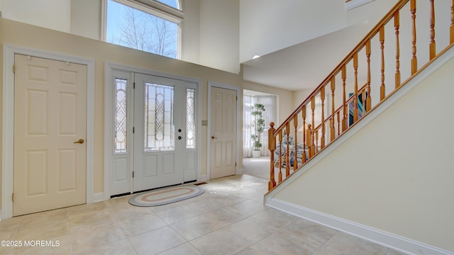 entryway with stairway, tile patterned floors, a towering ceiling, and baseboards