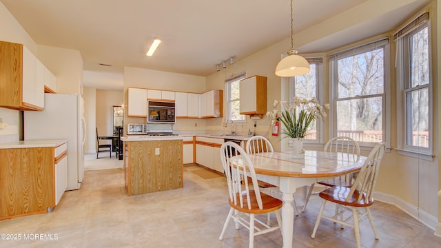 kitchen featuring a center island, light countertops, hanging light fixtures, a sink, and black microwave